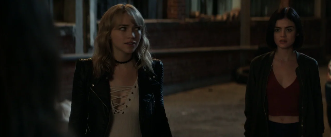 Truth or Dare (2018) movie still: medium — An outdoor urban space at night with a red brick wall in the background. Two young women stand in the…