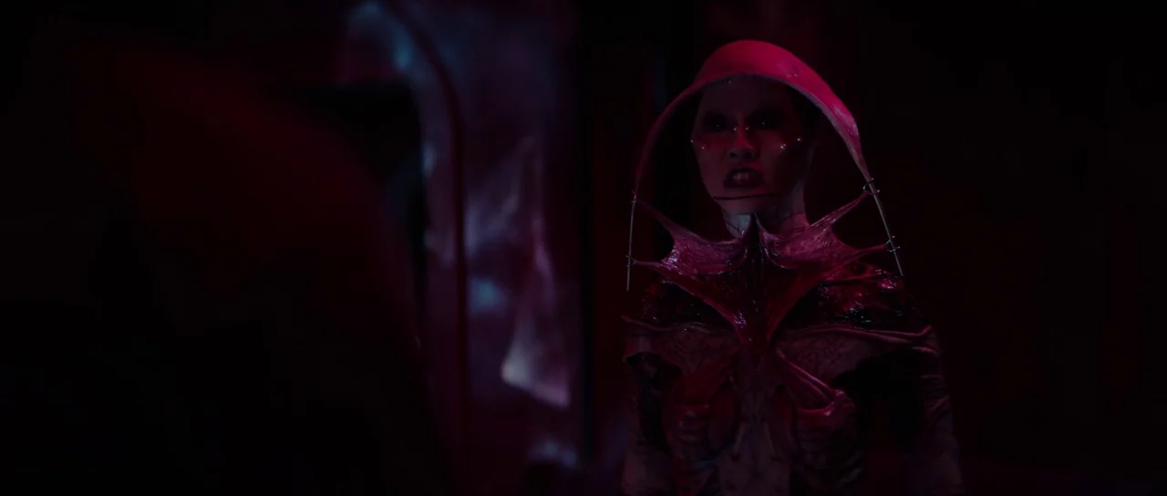Hellraiser (2022) movie still: medium — A dim, dark space characterized by deep red lighting and biological, alien-looking architecture. A female…