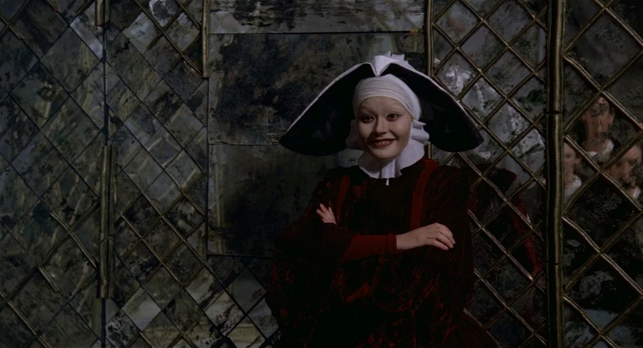 Fellini’s Casanova (1976) movie still: medium — A person in a historical costume stands before a large, grid-patterned antique mirrored wall. The…