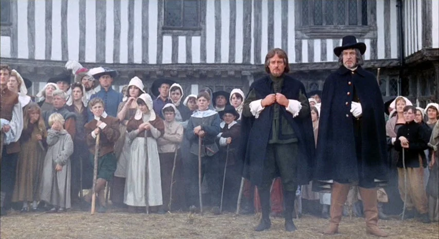 Witchfinder General (1968) movie still: fullbody — A group of people dressed in 17th-century style clothing stand before a timbered building. Two…