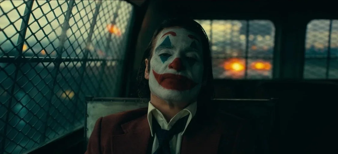 Joker: Folie à Deux (2024) movie still: medium — Inside a police transport vehicle with a metal wire partition separating front and back. A man…