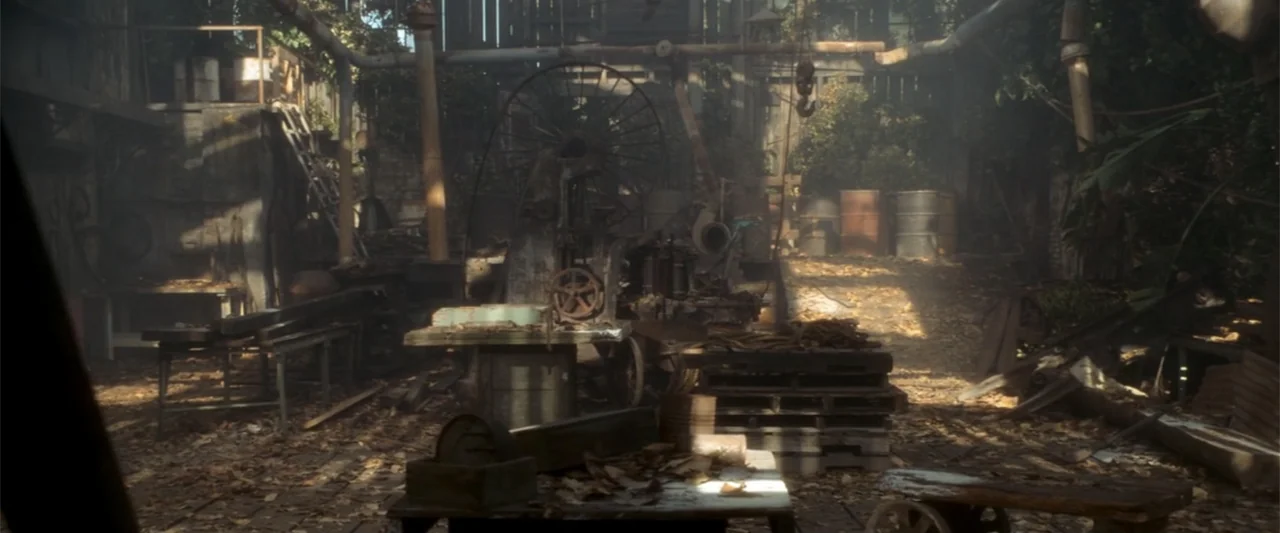 Anaconda (2025) movie still: establishing — An outdoor industrial area cluttered with rusted machinery and discarded barrels under dappled light.…
