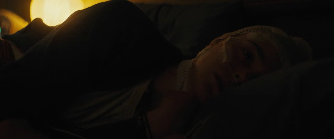 I Think We’re Alone Now (2018) movie still: closeup — A person lies in a dark room under soft, rumpled bed sheets. The subject's head is wrapped in…