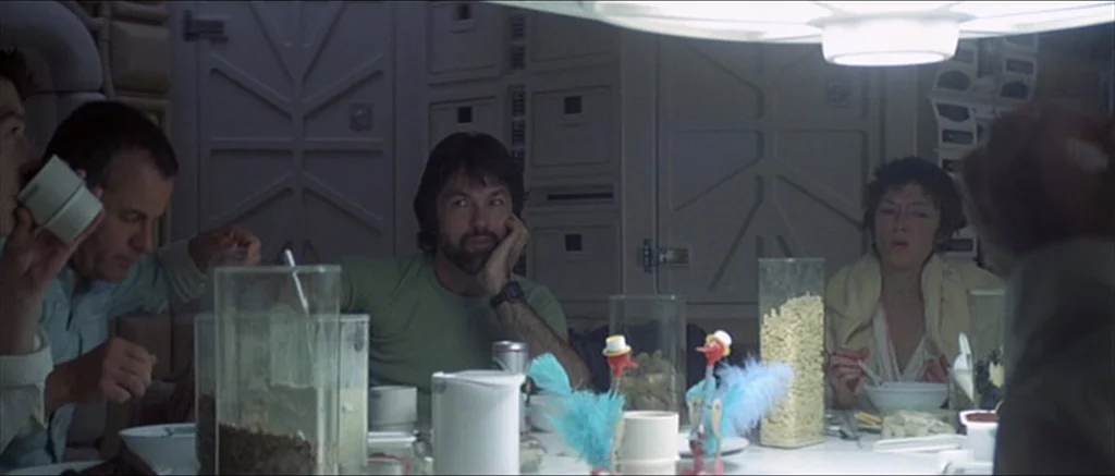Alien (1979) movie still: medium — A utilitarian spaceship mess hall features white panel walls with mechanical geometric textures. Three…