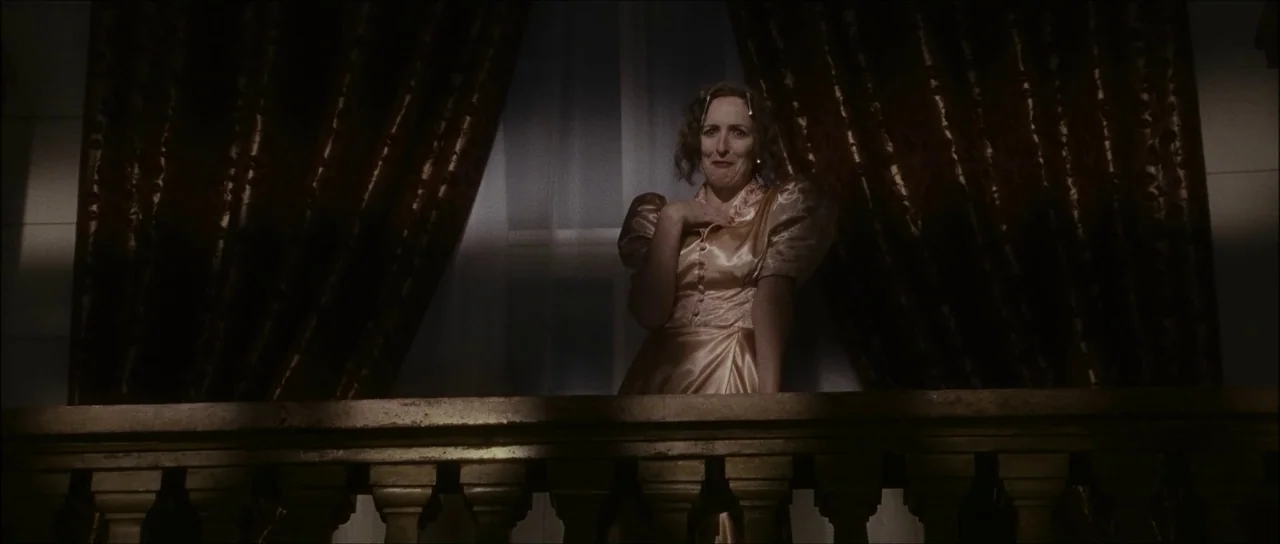 The Black Dahlia (2006) movie still: medium — A woman stands behind a stone railing framed by thick, draped curtains at night. She leans forward…