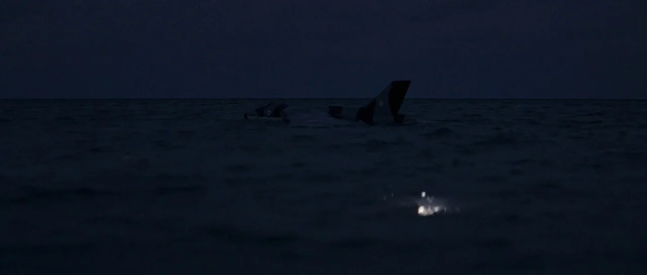 Thunderball (1965) movie still: wide — A partially submerged military aircraft drifts in a vast expanse of dark ocean at night. The tail fin and…