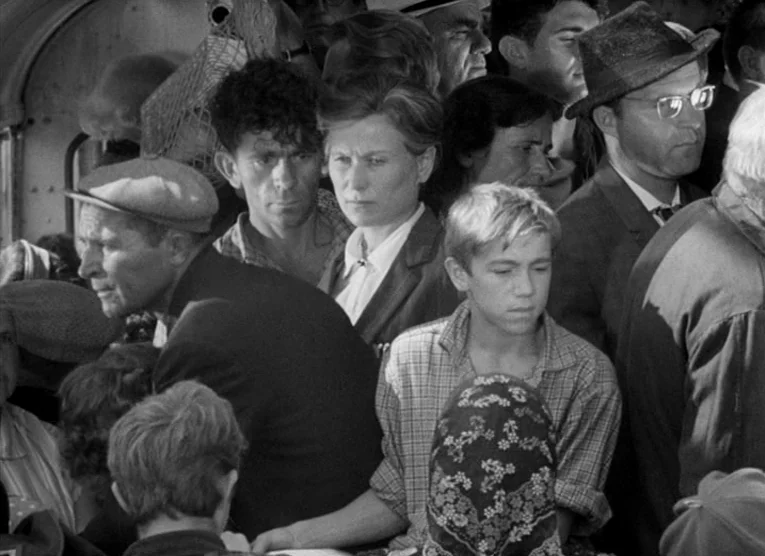 Wings (1966) movie still: medium — A dense group of passengers fills a crowded interior train car. They remain stationary while packed closely…