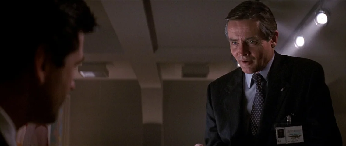 The Hunt for Red October (1990) movie still: medium — A dimly lit professional office with a drop ceiling and visible track lighting. A middle-aged…