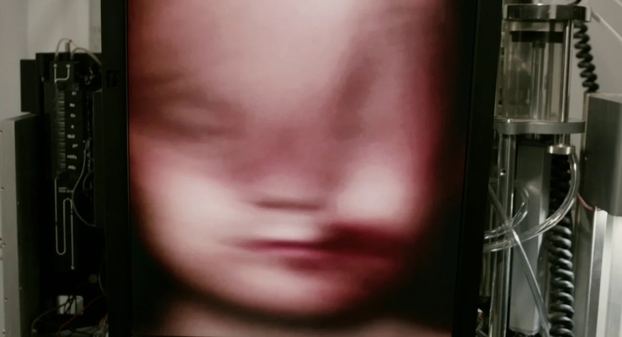 Antiviral (2012) movie still: closeup — A dark monitor displays a grainy, high-contrast ultrasound scan of a fetus. The surrounding laboratory…