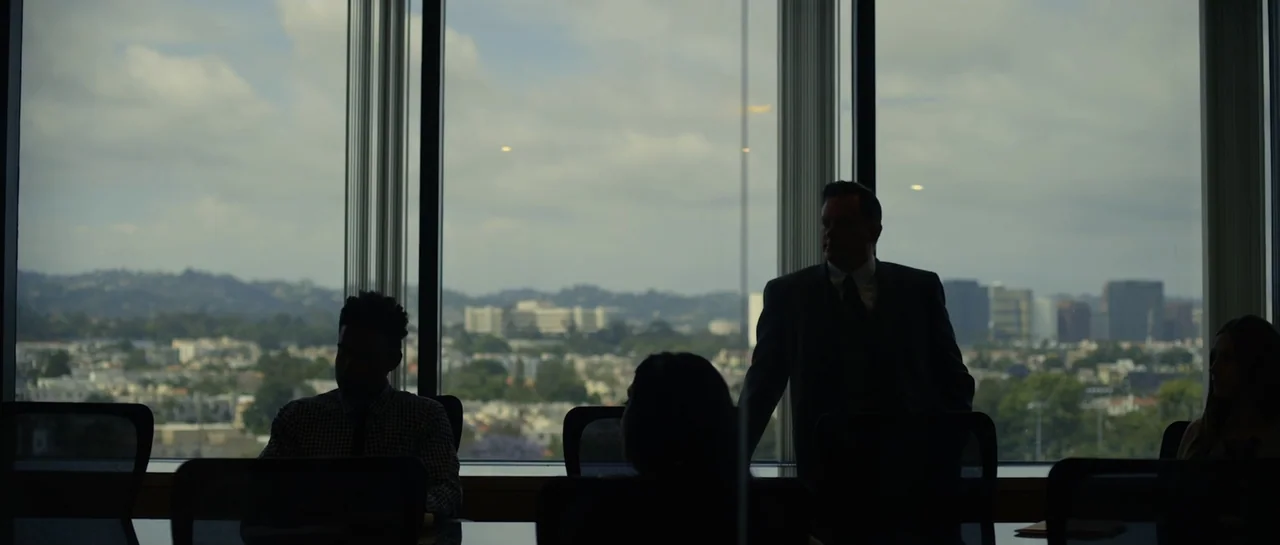 La presencia (2012) movie still: medium — A high-rise conference room overlooks a sprawling urban cityscape under an overcast sky. A group of…