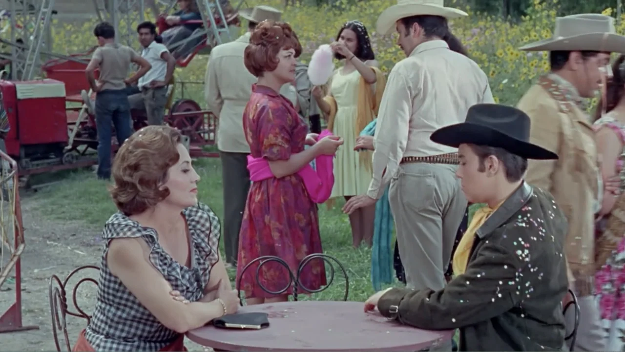Los Dos Rivales (1966) movie still: medium — A bustling outdoor fairground features people walking in the background near a red structure. A man and…