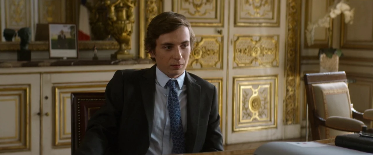 Nocturama (2016) movie still: medium — A formal office space features ornate gold-leaf wall panels and classic architectural moldings. A young man…