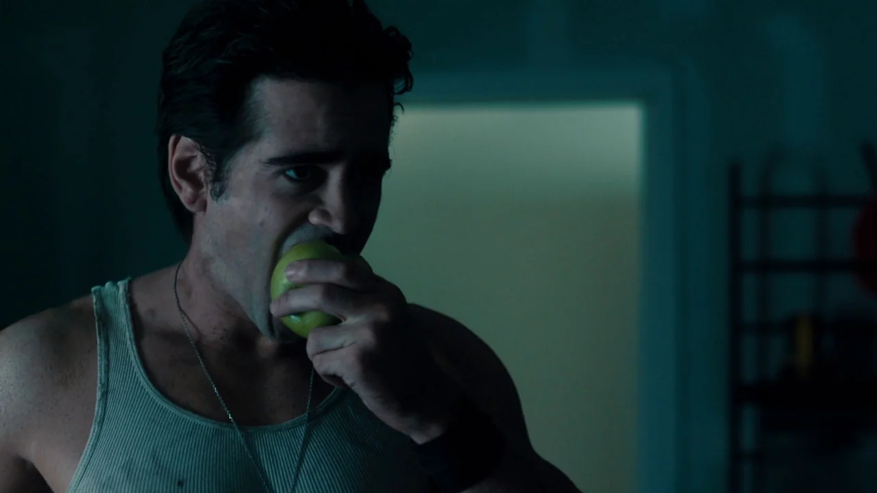 Fright Night (2011) movie still: closeup — A dark, dimly lit apartment with a faint light source in the background. A man wearing a tank top eats a…