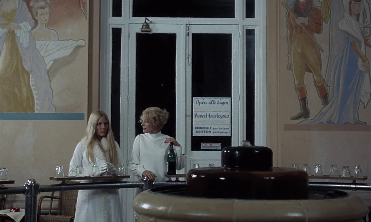 Daughters of Darkness (1971) movie still: medium — A quiet indoor mineral spring hall features murals on the walls and a central fountain. Two…