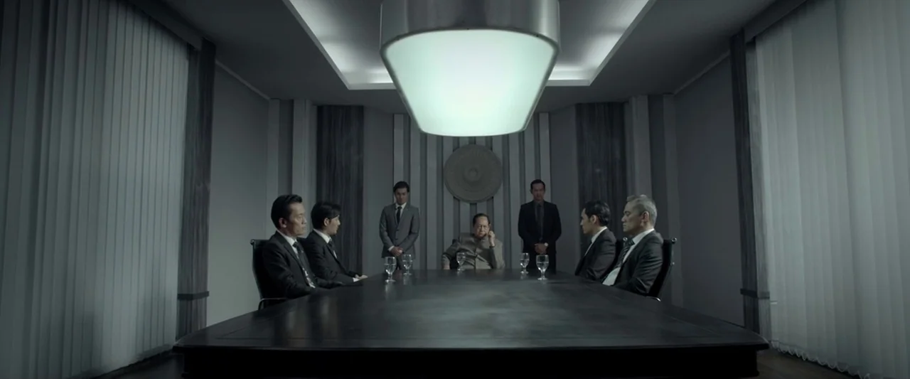 The Raid 2 (2014) movie still: wide — A sterile corporate meeting room features a massive dark table and minimalist gray walls. Seven men in suits…