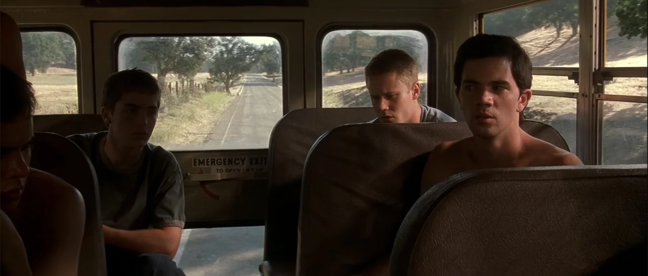 Jeepers Creepers 2 (2003) movie still: medium — A view from inside a bus shows three young men sitting on brown seats. Through the rear window, a…