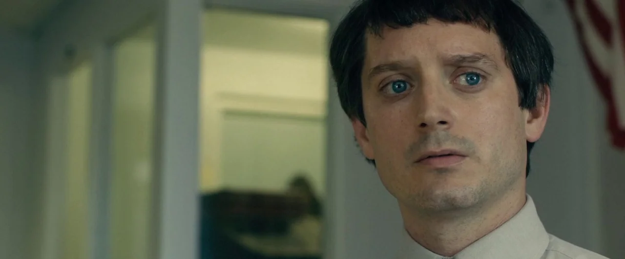 No Man of God (2021) movie still: closeup — An interior space with a glass partition and a glimpse of a blurry workspace. A man with short dark hair…