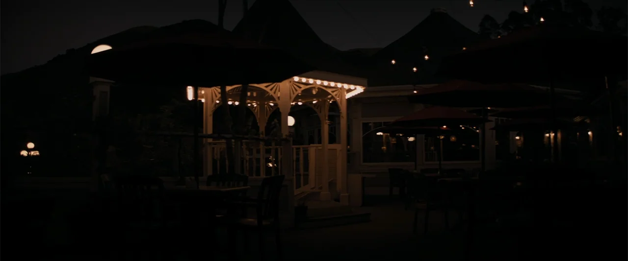 Destination Wedding (2018) movie still: wide — An outdoor dining patio at night features a central illuminated white gazebo structure. Dark, empty…