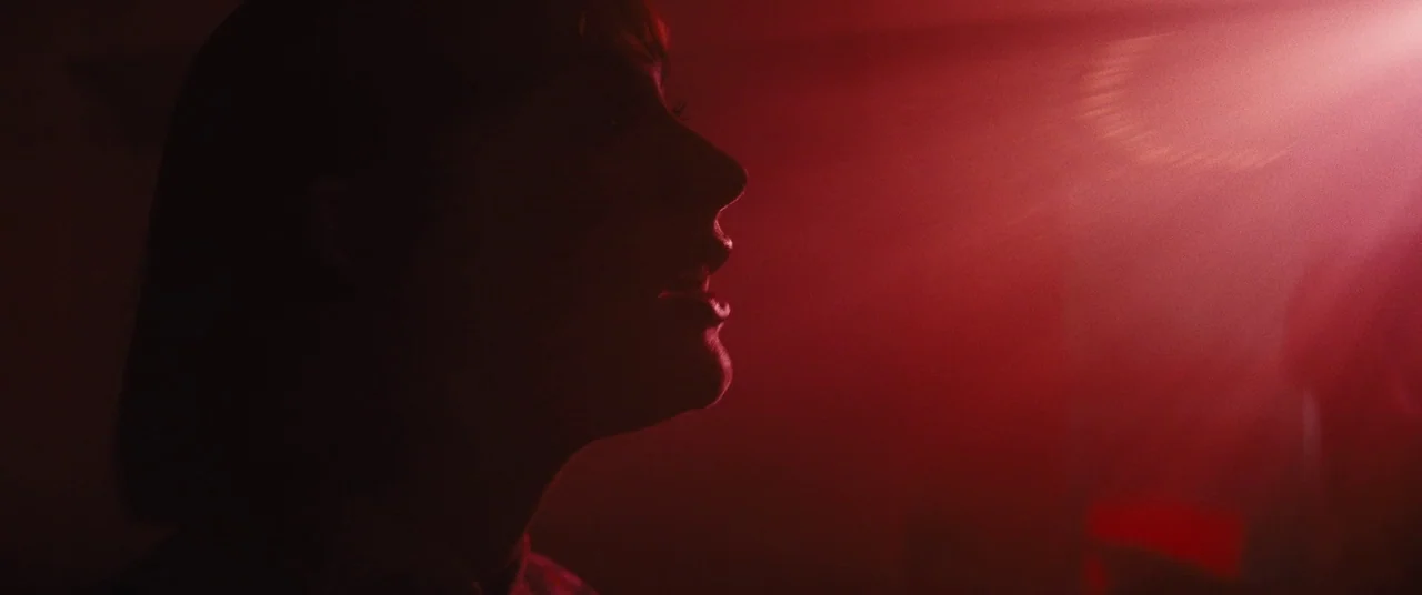 Daniel Isn’t Real movie still: closeup — A dark space is dominated by a sharp, volumetric beam of red light. A young woman's silhouette is visible…