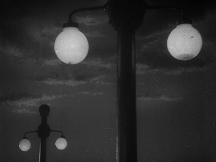 Anatomy of a Relationship (1976) movie still: establishing — Two ornate streetlamp posts rise against a dark night sky with faint cloud streaks. The…