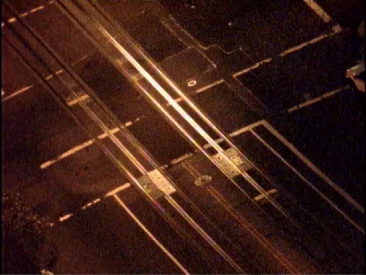 America Undercover: Life Afterlife (2000) movie still: establishing — An aerial view shows train tracks running across a dark asphalt road at night.…