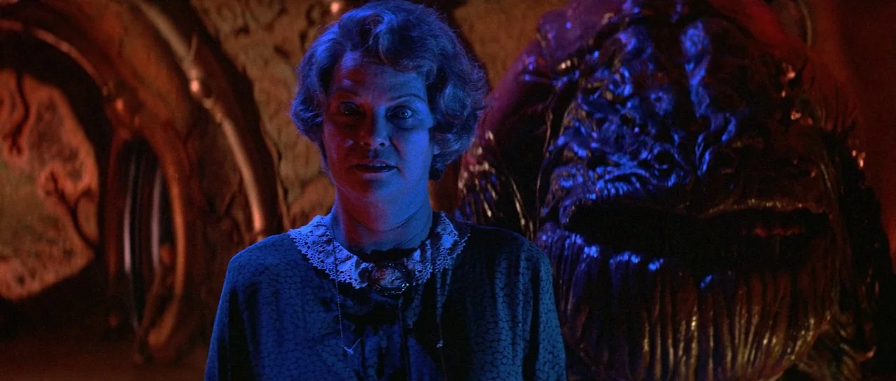 Invaders From Mars (1986) movie still: medium — A dimly lit cavern features organic, textured walls with deep red shadows and crevices. A…