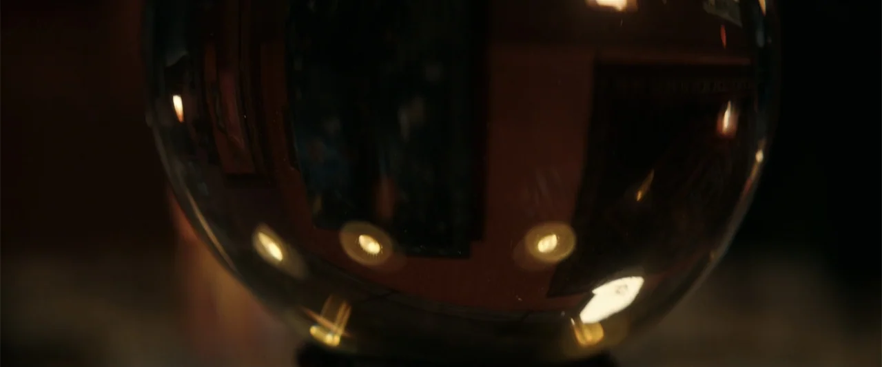 Hypnotic (2023) movie still: closeup — A dark indoor space contains a large, reflective glass sphere. The sphere captures a distorted image of a…