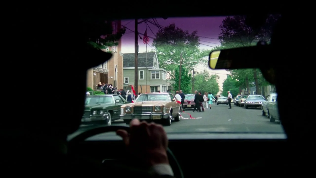Sorcerer (1977) movie still: wide — A suburban street in front of a church building where guests gather. A driver's perspective from inside a car…