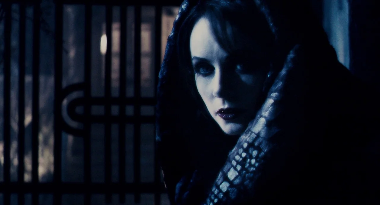 Repo! The Genetic Opera (2008) movie still: closeup — A woman stands before a dark iron gate at night in blue-toned shadow. She is positioned to the…
