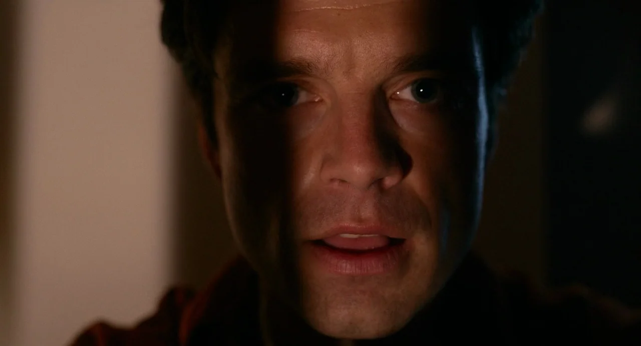 Fresh (2022) movie still: closeup — The face of a middle-aged man is illuminated from the side in darkness. He looks forward with his mouth slightly…
