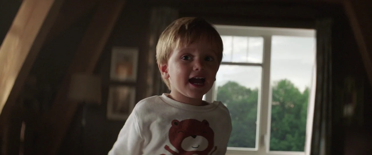 Pet Sematary (2019) movie still: medium — An interior bedroom space features slanted ceiling beams and a large window facing greenery. A young boy…