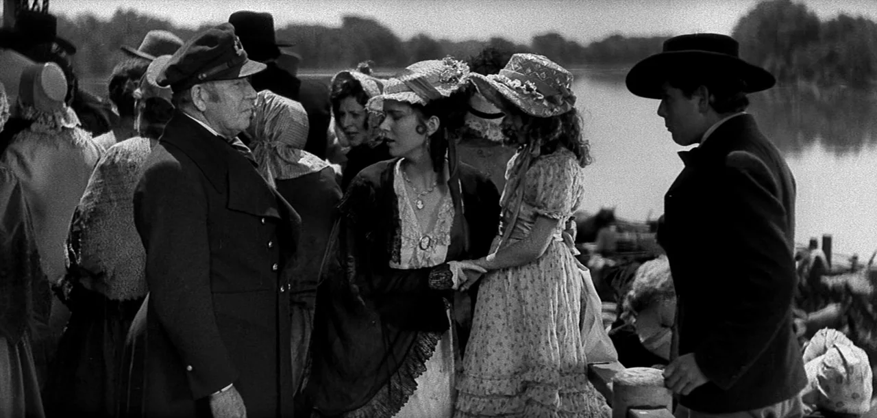 The Big Trail (1930) movie still: medium — A bustling nineteenth-century waterfront dock filled with people wearing period-appropriate hats and…