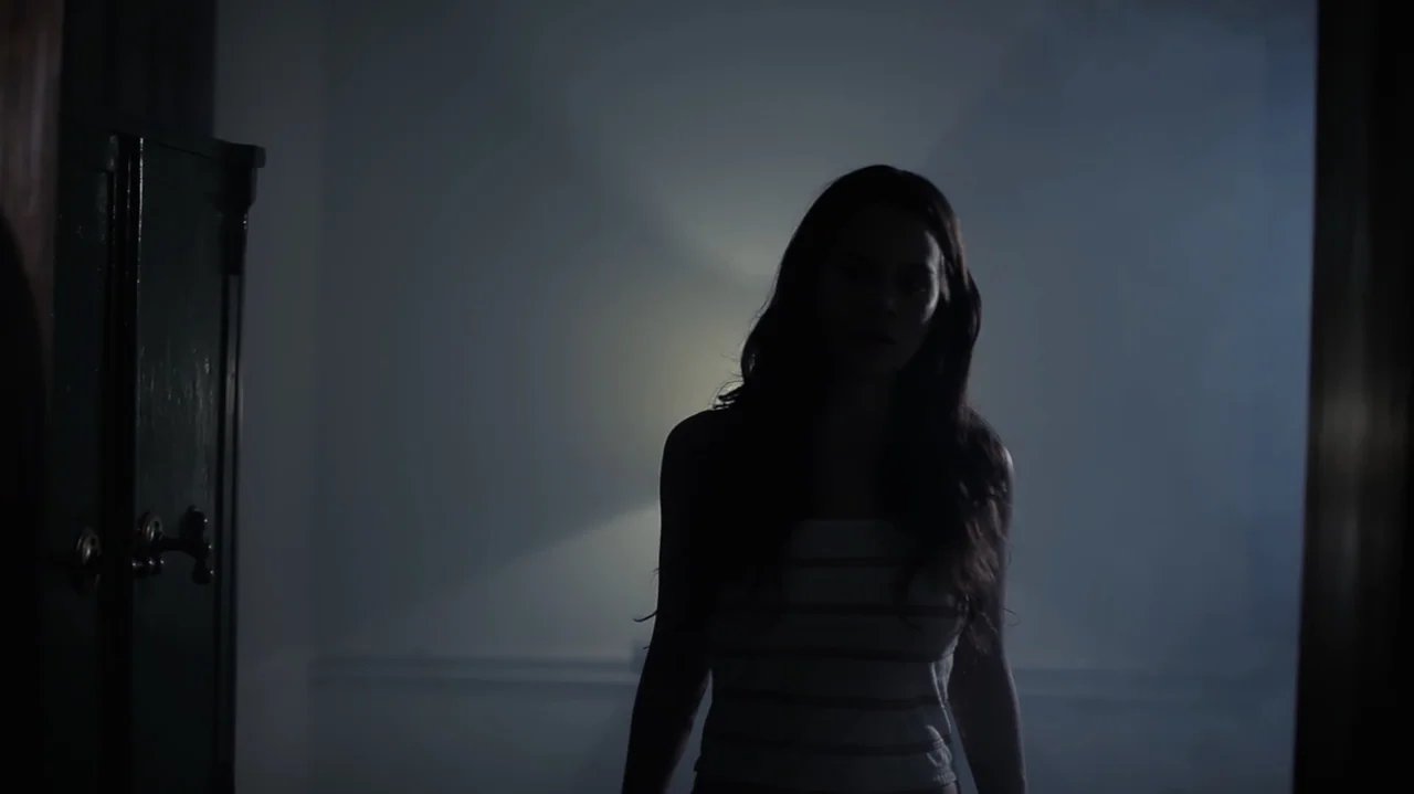Still Life (2013) movie still: medium — A dimly lit interior hallway filled with faint haze or smoke. A lone woman stands in the center foreground…