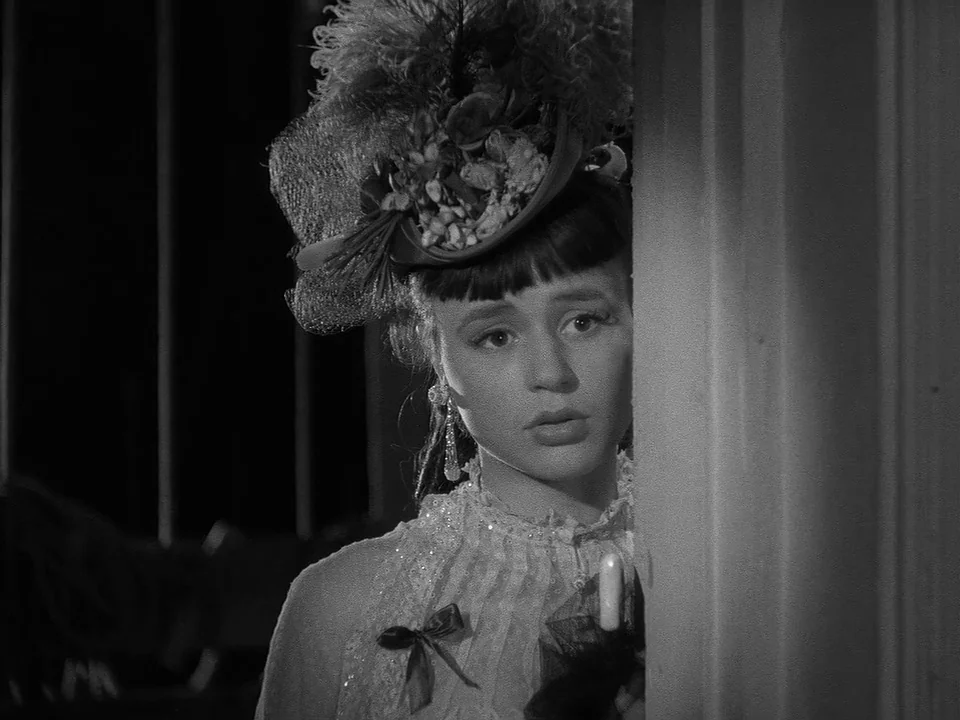 Sawdust and Tinsel (1953) movie still: closeup — A woman stands partly obscured behind a white wooden door frame in a dark room. She looks toward…