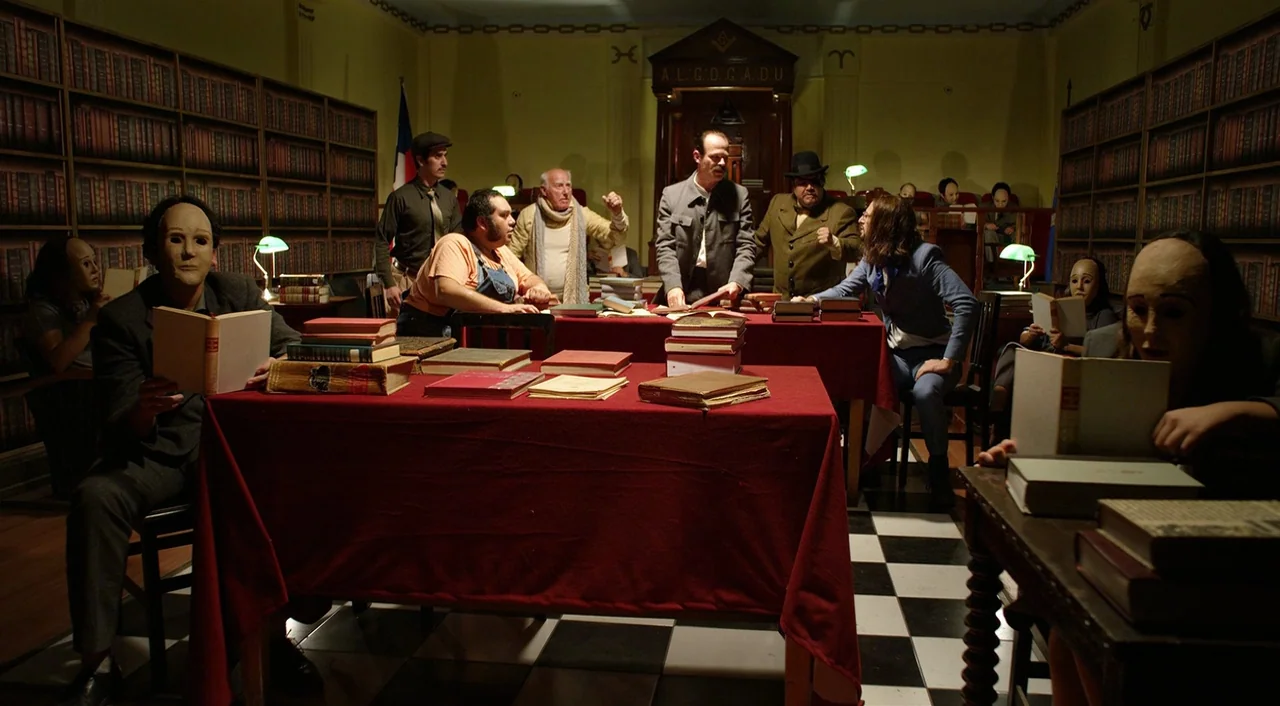 Dance of Reality (2013) movie still: wide — A dimly lit room functions as a meeting space with red-covered tables and bookshelves. Several men…