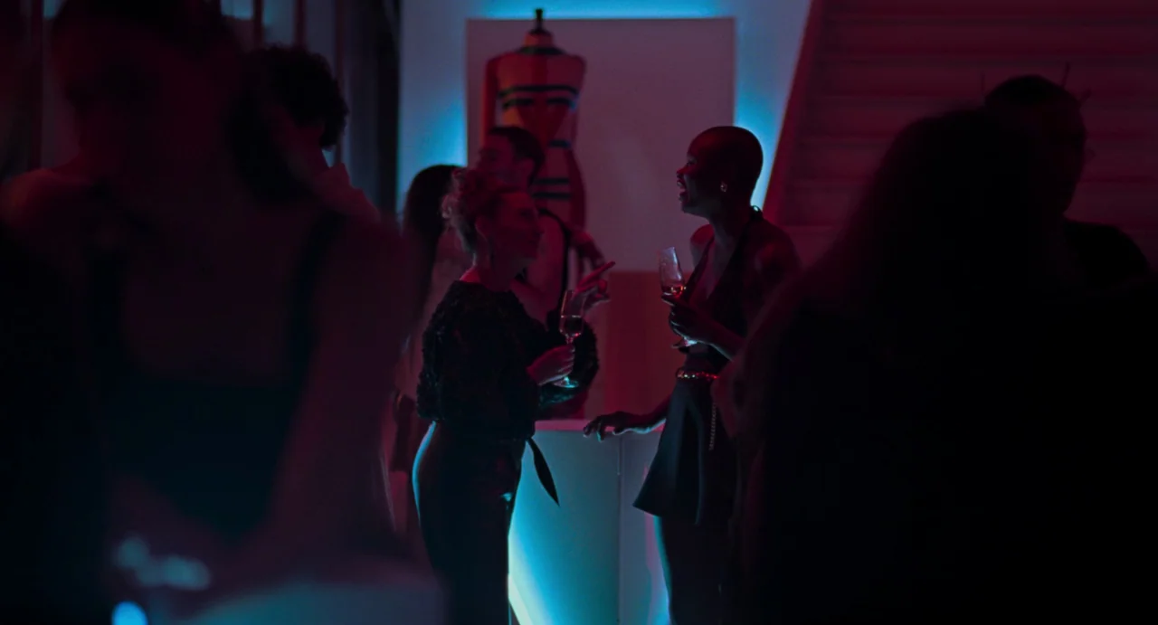 La Abuela (2021) movie still: medium — An interior space features a backlit mannequin display and a central counter area. Two women hold wine…