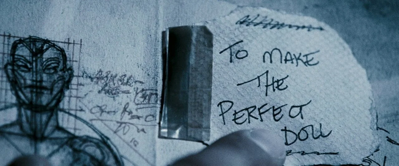 Dead Silence (2007) movie still: closeup — A torn scrap of paper is taped onto a surface featuring a detailed sketch. The handwritten note reads to…