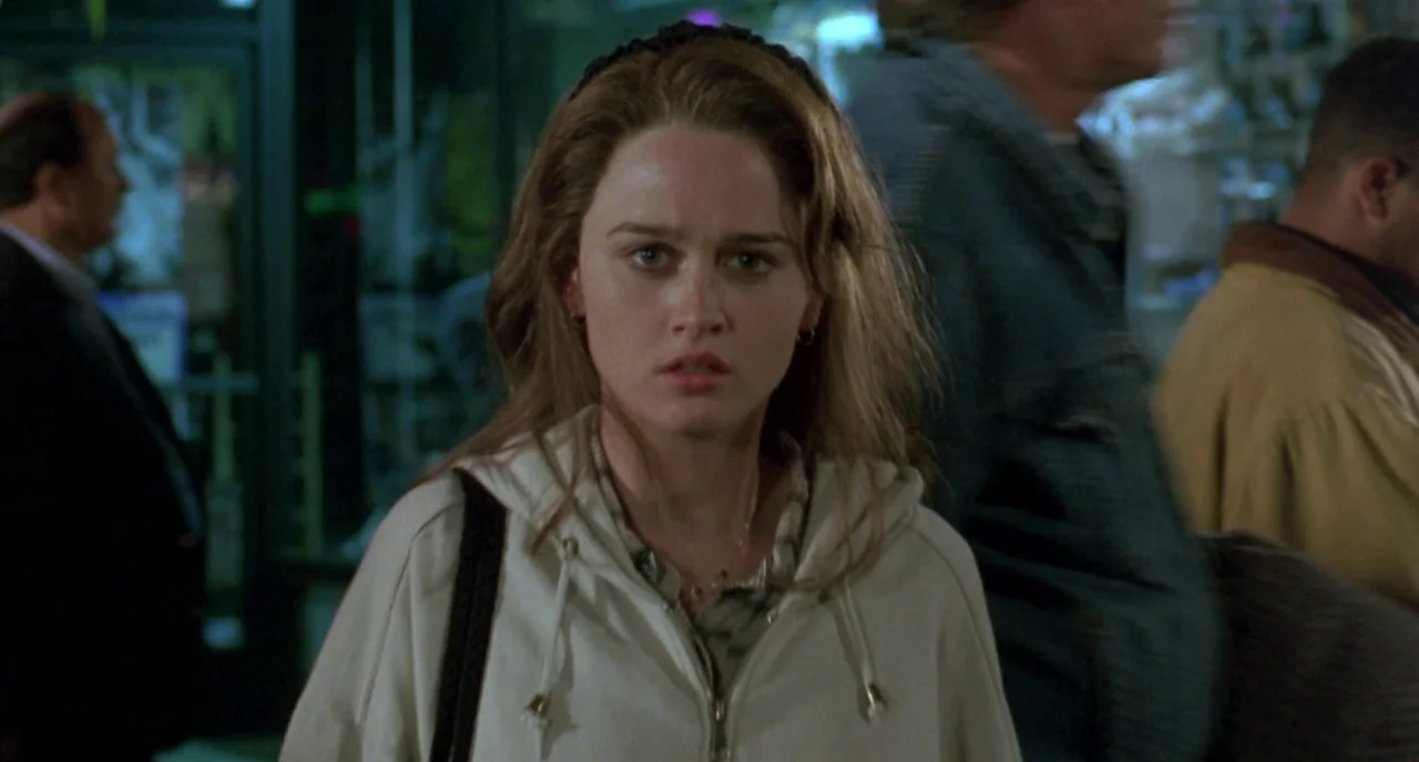 The Craft (1996) movie still: medium — A woman stands in the exterior area of a retail space at night. She looks forward while other figures are…