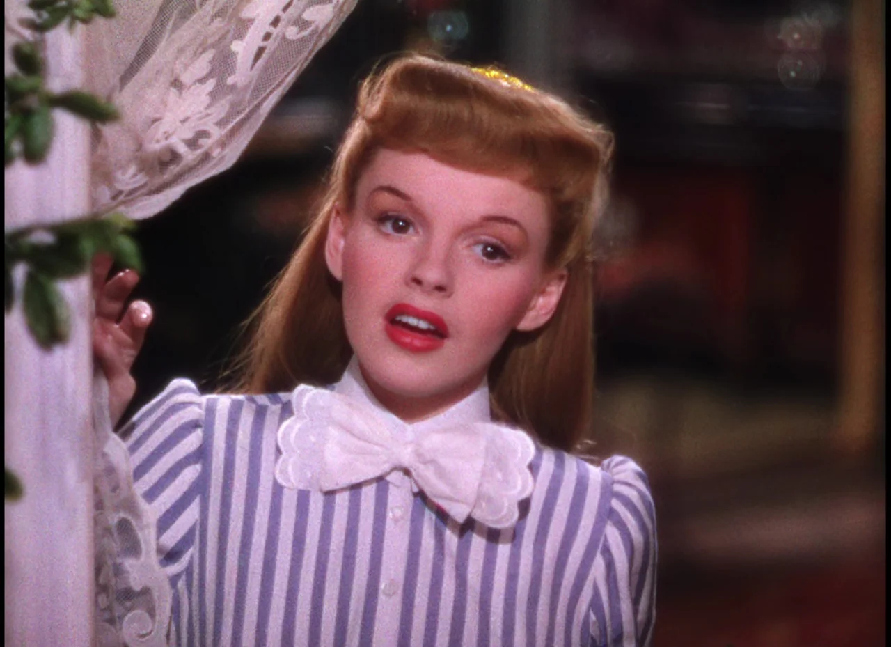 Meet Me In St. Louis (1944) movie still: closeup — A well-lit indoor space featuring a draped white lace curtain in the foreground. A young woman…