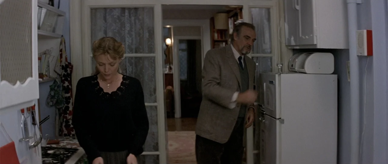 The Russia House (1990) movie still: medium — A light-walled home interior with glass-paned doors leading to an adjacent living area. A woman and an…