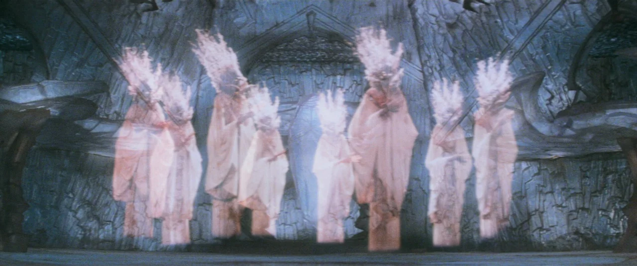 The Dark Crystal (1982) movie still: wide — A stone hall features carved, textured walls and a high, vaulted ceiling. Several translucent, glowing…