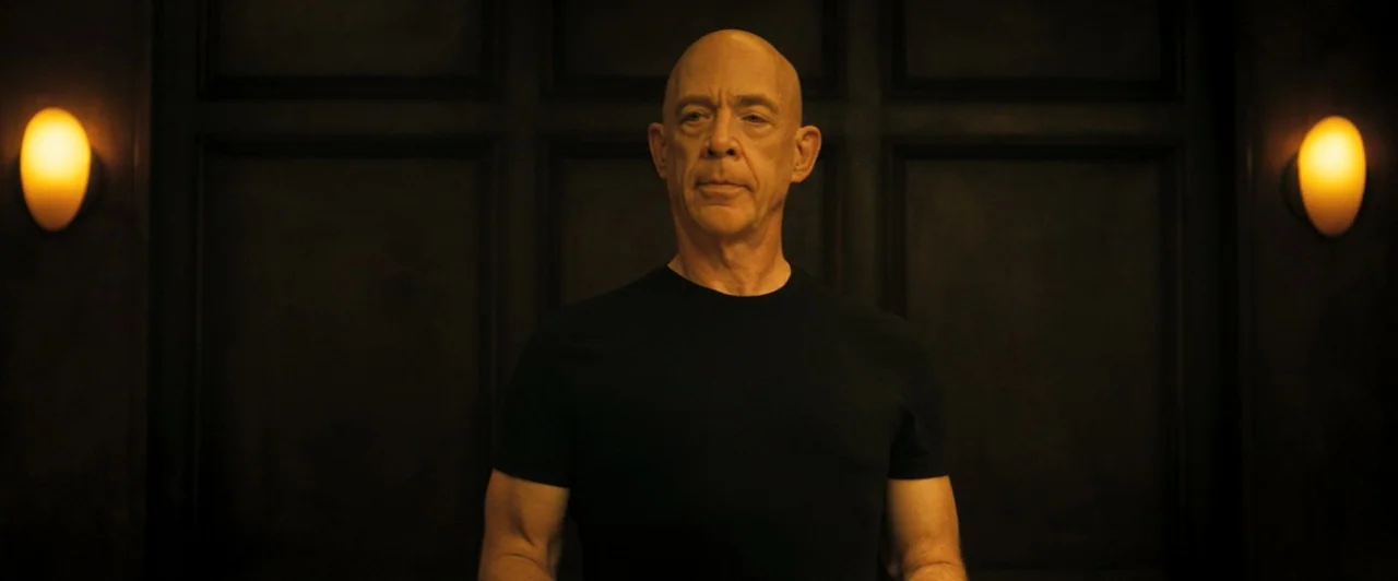 Whiplash (2014) movie still: medium — A dark, wood-panelled wall serves as the backdrop for a dimly lit indoor space. A bald man stands centrally in…