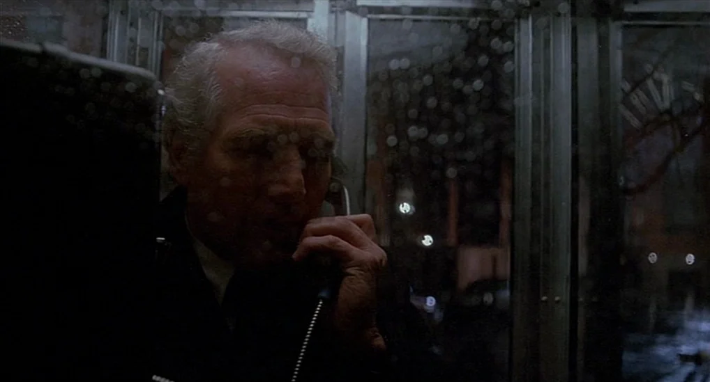 The Verdict (1982) movie still: closeup — An elderly man is inside a dark, rainy telephone booth at night. He holds a telephone receiver to his ear…