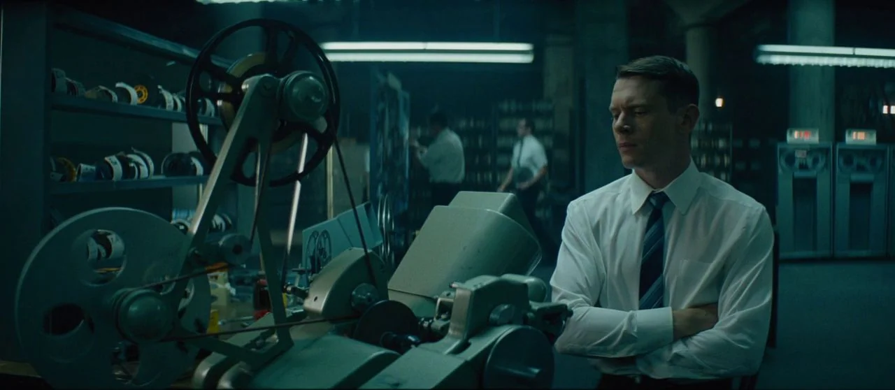 Seberg (2019) movie still: medium — A dimly lit room filled with industrial archive equipment and metal shelving units. A man stands in the…