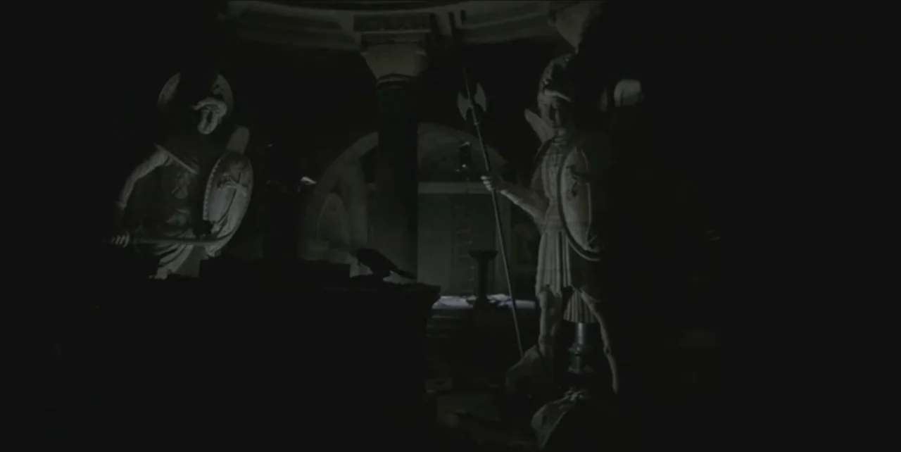 Exorcist: The Beginning (2004) movie still: medium — A dark subterranean crypt features a central altar flanked by two carved statues. The statues…