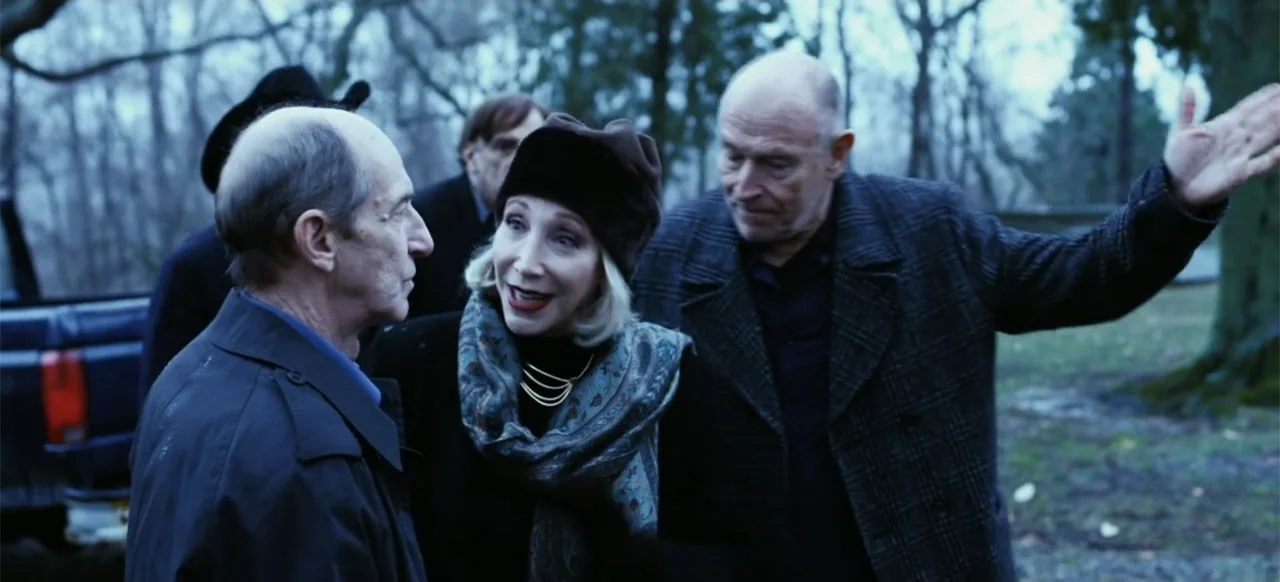 The Russian Bride (2019) movie still: medium — An outdoor park area with leafless trees and a dark vehicle parked nearby. Three older adults in…