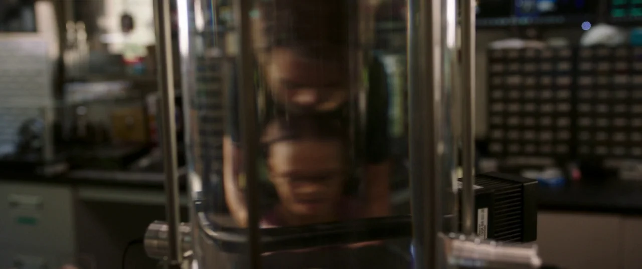 A Wrinkle In Time (2018) movie still: medium — A dark laboratory workspace with shelves of equipment visible in the blurred background. A young…