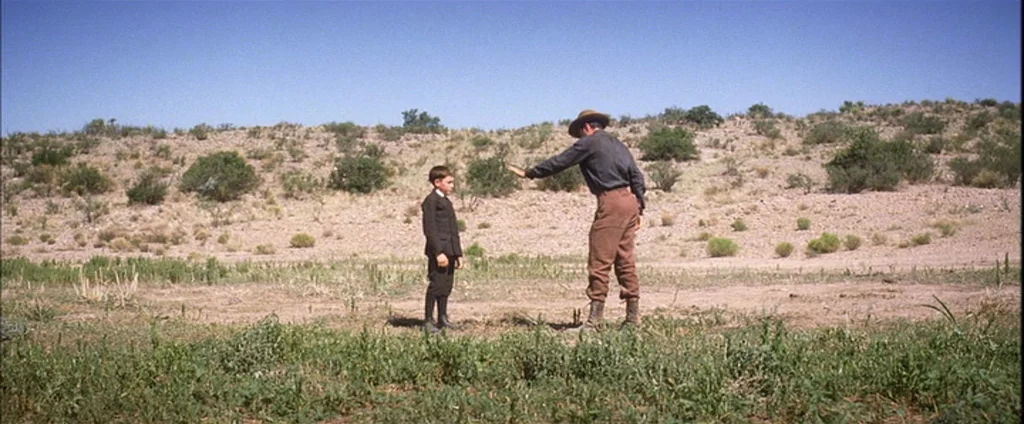 There Will Be Blood (2007) movie still: fullbody — An arid landscape features sparse desert vegetation and low hills under a clear sky. A man…