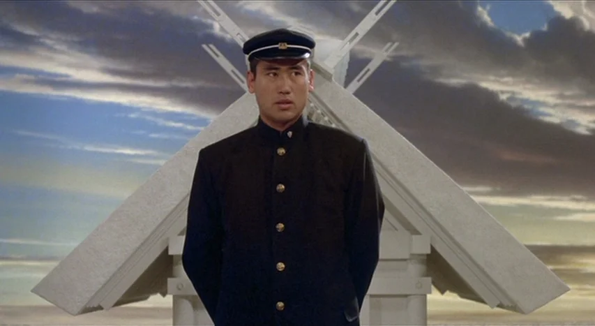 Mishima: A Life in Four Chapters (1985) movie still: medium — A man in a military-style uniform stands before a stylized, geometric white…