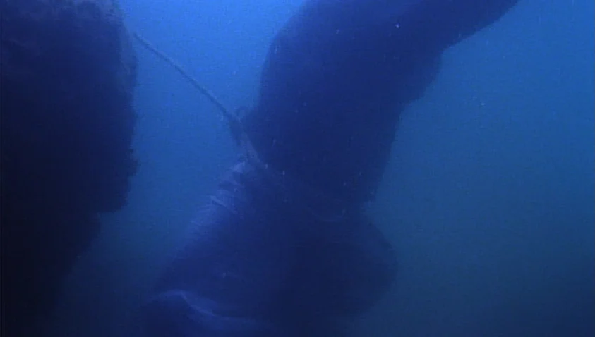 A Bay of Blood (1971) movie still: medium — A dark, submerged body floats in deep blue underwater space. The figure is tethered to a thin rope that…